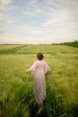 Fototapeta na wymiar Portrait of a overweight woman in a pink dress. A woman is standing in a green wheat field.