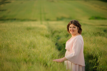 Fototapeta na wymiar Portrait of a overweight woman in a pink dress. A woman is standing in a green wheat field.