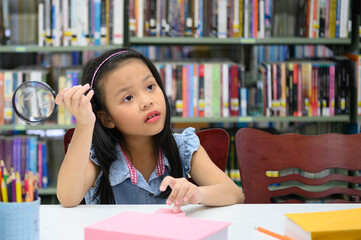 Asian girl holding magnifying glass and thinking in library at school. Education and learning concept