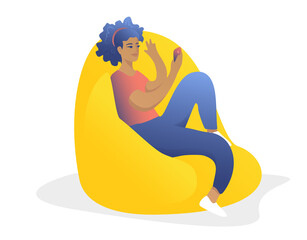 Young happy girl with an afro is sitting in a bag-chair with a telephone. People chat online. Rest at home with friends.