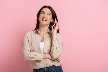 Beautiful smiling woman talking on smartphone on pink background