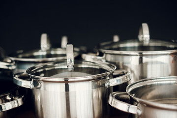 Set of kitchen metallic pans standing on wooden countertop on dark background