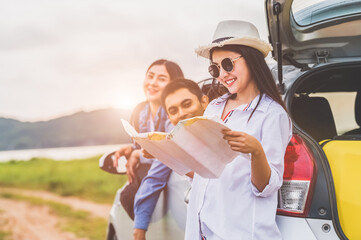 Happy Asian woman and her friends standing by car. Young girl having fun during road trip