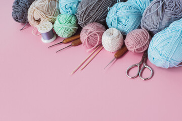 Women's hobby. Multicolored skeins, needles, hooks on the pink background. Conept of sewing, crochet and knitting.	