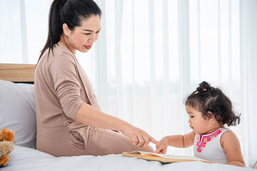 Asian mother teaching girls daughter to reading books in house