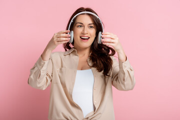 Positive woman holding wireless headphones on pink background
