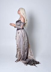 full length portrait of blonde girl wearing long torn, old wedding gown. standing pose on a studio background.