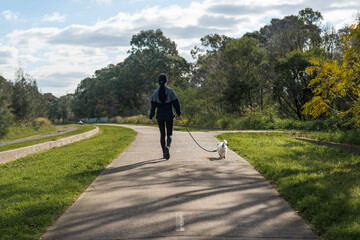 Girl in surgical mask in casual urban athletic wear walking with pet dog on a leash at a nature...
