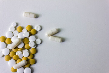 A lot of white and yellow pills and capsules on a white background