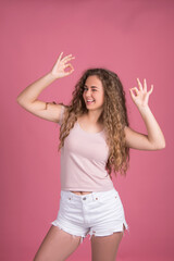 Happy girl with long curly hair, smiling holding bottle package of hair care product. Mockup with copy space, isolated on pink