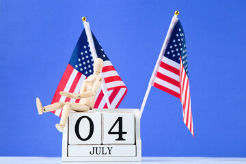Independence Day concept. American flags with cube calendar and wooden figure on blue background
