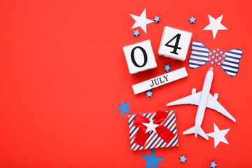 Independence Day concept. Cube calendar with gift box, airplane model and paper stars on red background