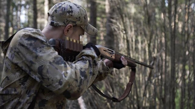 Man hunter takes aim with rifle. Hunter with hunting weapons in the autumn forest. Man in comfortable camouflage clothes hunter outdoor in forest hunting alone.