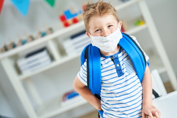 Adorable little boy in kindergarten with mask on due to coronavirus pandemic