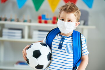 Adorable little boy in kindergarten with mask on due to coronavirus pandemic