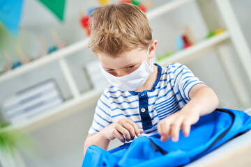 Adorable little boy in kindergarten with mask on due to coronavirus pandemic