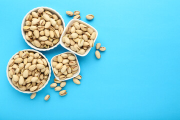 Fototapeta na wymiar Tasty pistachios in bowls on blue background