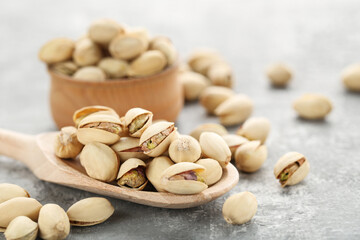 Tasty pistachios in bowl and spoon on grey background