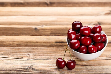 Sweet cherries in bowl on brown wooden table