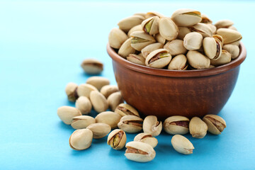 Tasty pistachios in bowl on blue background