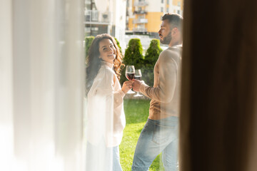 selective focus of man and happy woman standing outside and holding glasses of red wine