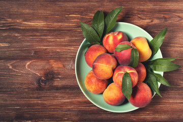 Fresh peaches with green leafs in plate on brown wooden table