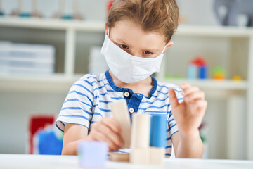 Adorable little boy in kindergarten with mask on due to coronavirus pandemic