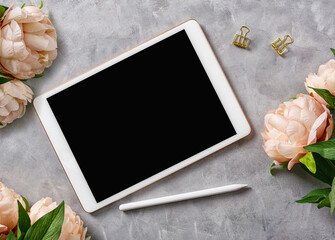 Flat lay top view mockup: digital tablet with pencil and flowers on grey background. Text space