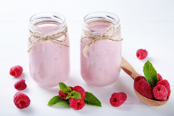 Raspberry smoothie in glass jars and spoon on white wooden table