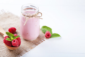 Raspberry smoothie in glass jar with spoon on white wooden table