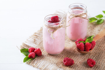 Raspberry smoothie in glass jars and spoon on white wooden table