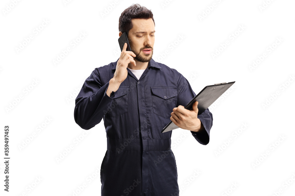 Wall mural Male worker in a blue uniform talking on a mobile phone and looking at a docment