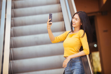 woman walking and using a smart phone on escalator in a sunny summer day