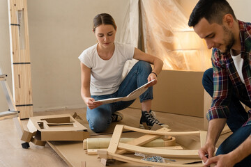 Happy Smiling Couple Collects Furniture as a Team. Girl Helps to Assemble Chair Details. Moving to...
