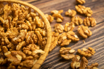 Peeled walnuts in a wicker basket and peeled walnuts scattered on a wooden table. Healthy diet. Fitness diet. Close up.