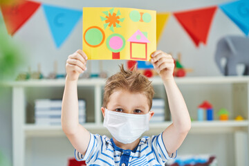 Adorable little boy in kindergarten with mask on due to coronavirus pandemic