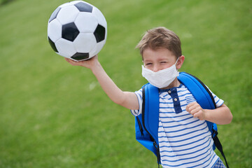 Adorable little boy with football and protective mask on the field