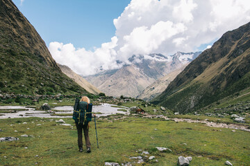 Back view of female tourist with travel backpack enjoying beautiful scenery of environment of mountains covered clouds.Young woman hiker exploring wilderness nature during wanderlust in Salkantay