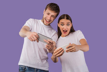 Excited couple using mobile phones on purple background