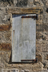 Grey Wooden Shutter Closed over Window in Rough Textured Stone Wall 