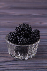 Small glass pot overfilled with blackberries. Close-up. Grey wooden background.