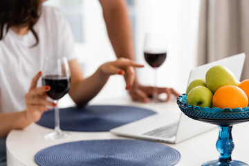 selective focus of fruits near wine glasses and freelancer pointing with finger at laptop