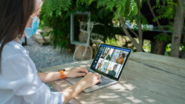 New Normal And Social Distancing After Covid Epidemic Concept.young Smart Asian Female Watching Laptop Meeting Business Team Or Webinar Course Online With Face Shield Or Mask Protection At Coffee Shop