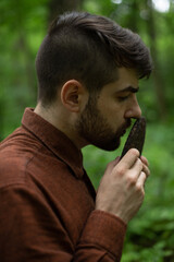 Profile of bearded man smelling dry disk of shu puer in summer forest