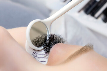 Eyelash extension procedure. Beautiful woman with long eyelashes in a beauty salon. Eyelashes close up. a mirror in the hands of a master