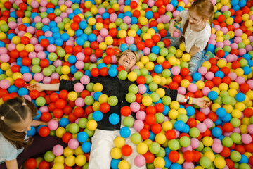 Fototapeta na wymiar Children with mother lying among colorful balls