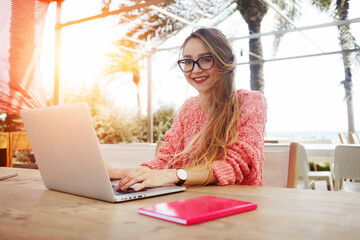 Smiling female student is looking at camera during work on portable net-book, while relaxing in...