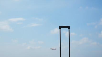 Handle from a suitcase against the blue sky with a plane taking off. Travel concept.