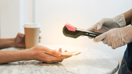 Customer hand in gloves use phone scan to pay money in coffee shop