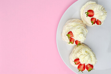 Top view of meringue cakes with cream and halves of strawberries on the plate on a pink background with copy space. Delicious dessert for candy bar. 